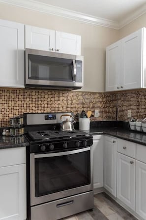 A kitchen with white cabinets, a stainless steel microwave, a gas stove, and a tiled backsplash.