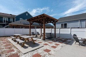 Un jardin avec une pergola en bois, des tables de pique-nique et des sièges d’extérieur.