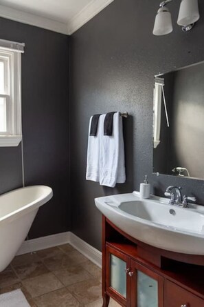 A bathroom with a white bathtub, a wooden vanity with a mirror, and two towels hanging on the wall. - Large Home w/ Back Yard Oasis | Perfect for Groups (New Orleans)