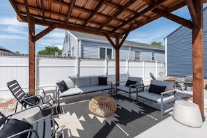 A covered outdoor seating area with a sofa, chairs, and a round table.