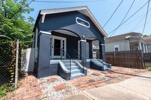 A two-story house with a dark blue exterior, a front porch with steps, and a small front yard with a brick pathway and gravel.