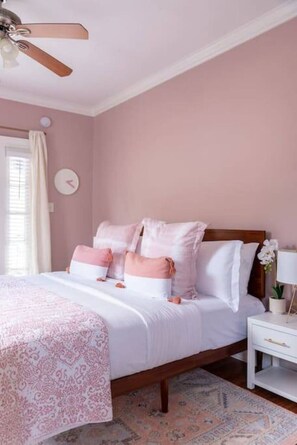 A bedroom with a bed, a nightstand, a clock, and a ceiling fan.