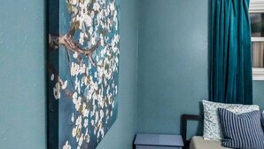 A bedroom with teal walls, a large floral artwork, a bed with blue and white pillows, and a window with teal curtains. - Large Home w/ Back Yard Oasis | Perfect for Groups (New Orleans)