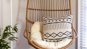 A hanging chair with a cushion and a patterned pillow in a room with a painting on the wall and a floor lamp. - Large Home w/ Back Yard Oasis | Perfect for Groups (New Orleans)