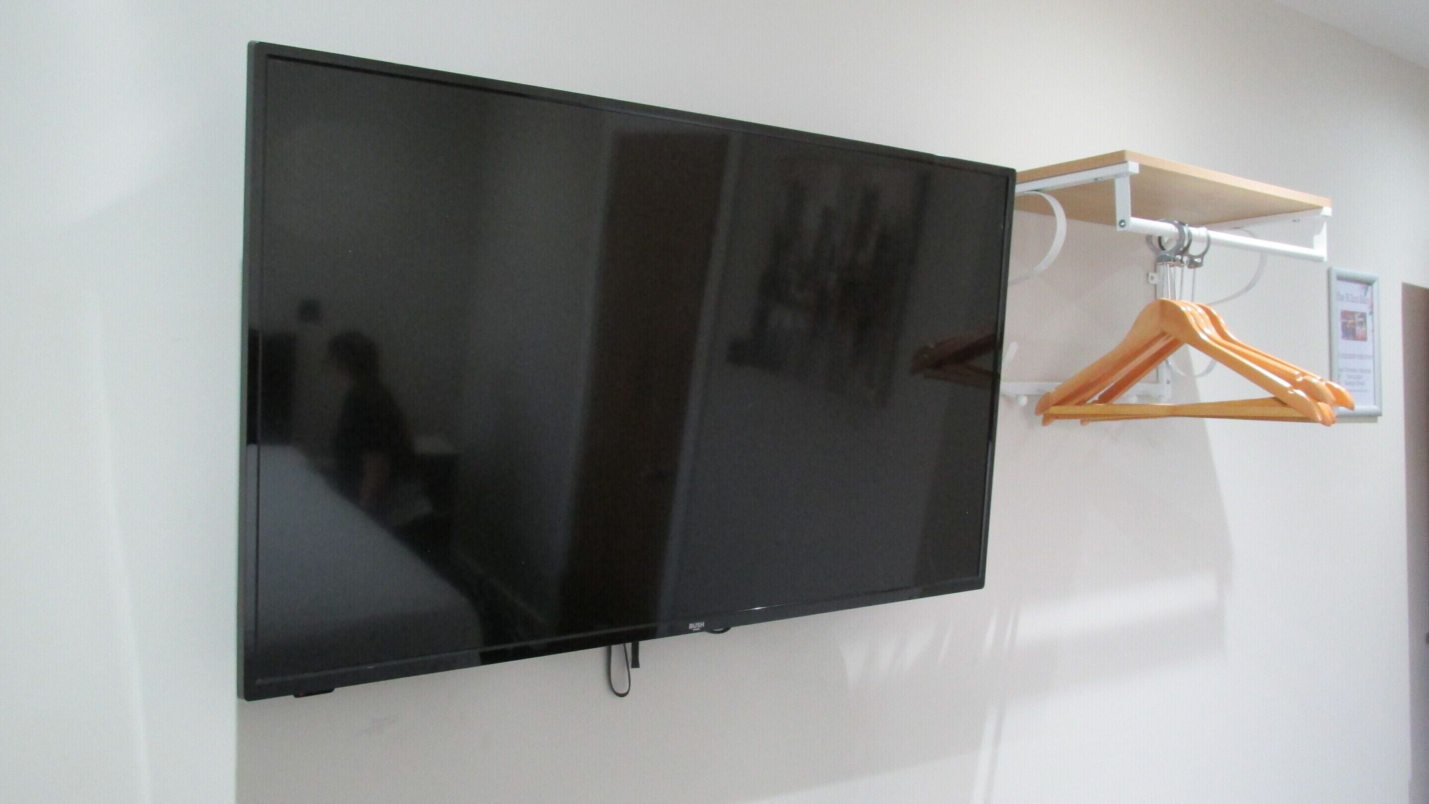 A flat-screen TV mounted on a wall with a white shelf above it.