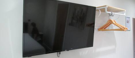 A flat-screen TV mounted on a wall with a white shelf above it.