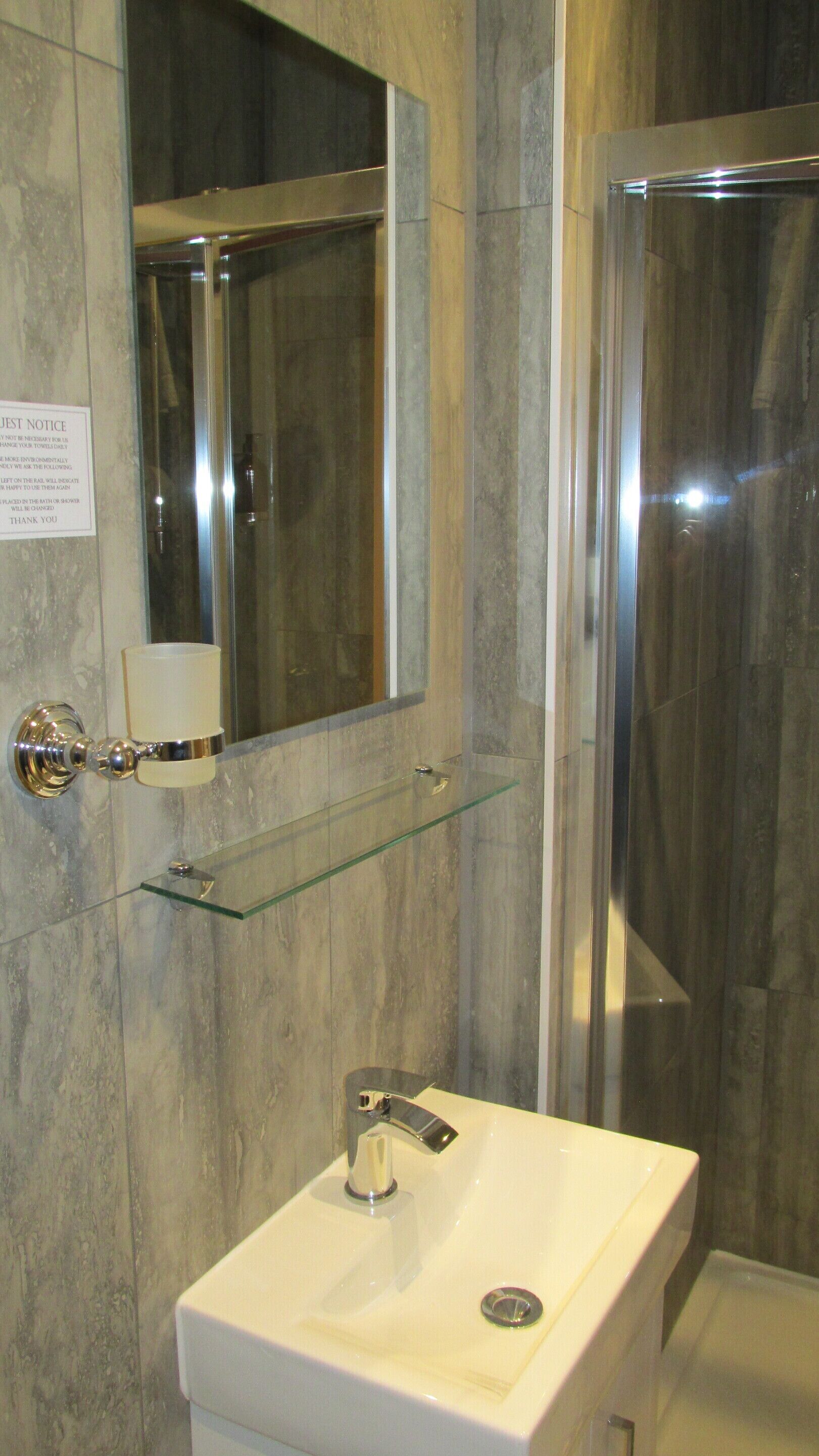 Un baño con pared de mármol, estante de vidrio, lavamanos blanco, espejo y cabina de ducha.