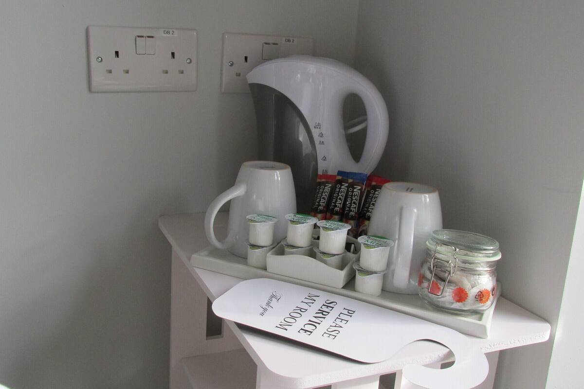A bathroom counter with a coffee maker, Nescafe capsules, and a jar of sugar.