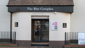 Entrada do Hotel Ritz Complex, com toldo preto, porta de vidro e uma placa de identificação.