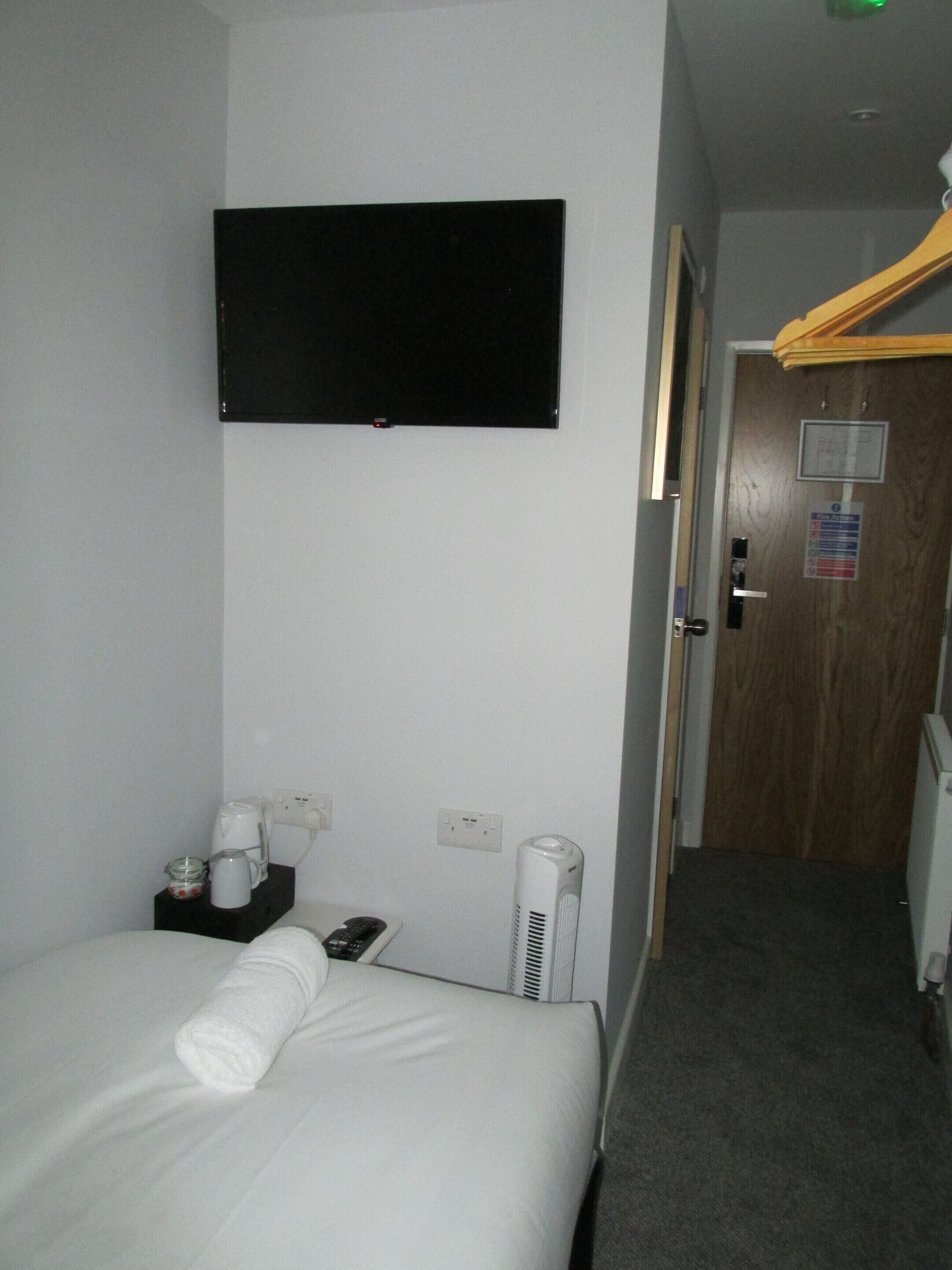 A hotel room with a bed, a flat-screen TV mounted on the wall, a coffee maker, a remote control, and a heater.