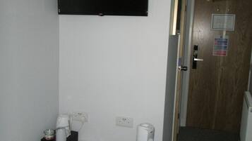 A hotel room with a bed, a flat-screen TV mounted on the wall, a coffee maker, a remote control, and a heater.