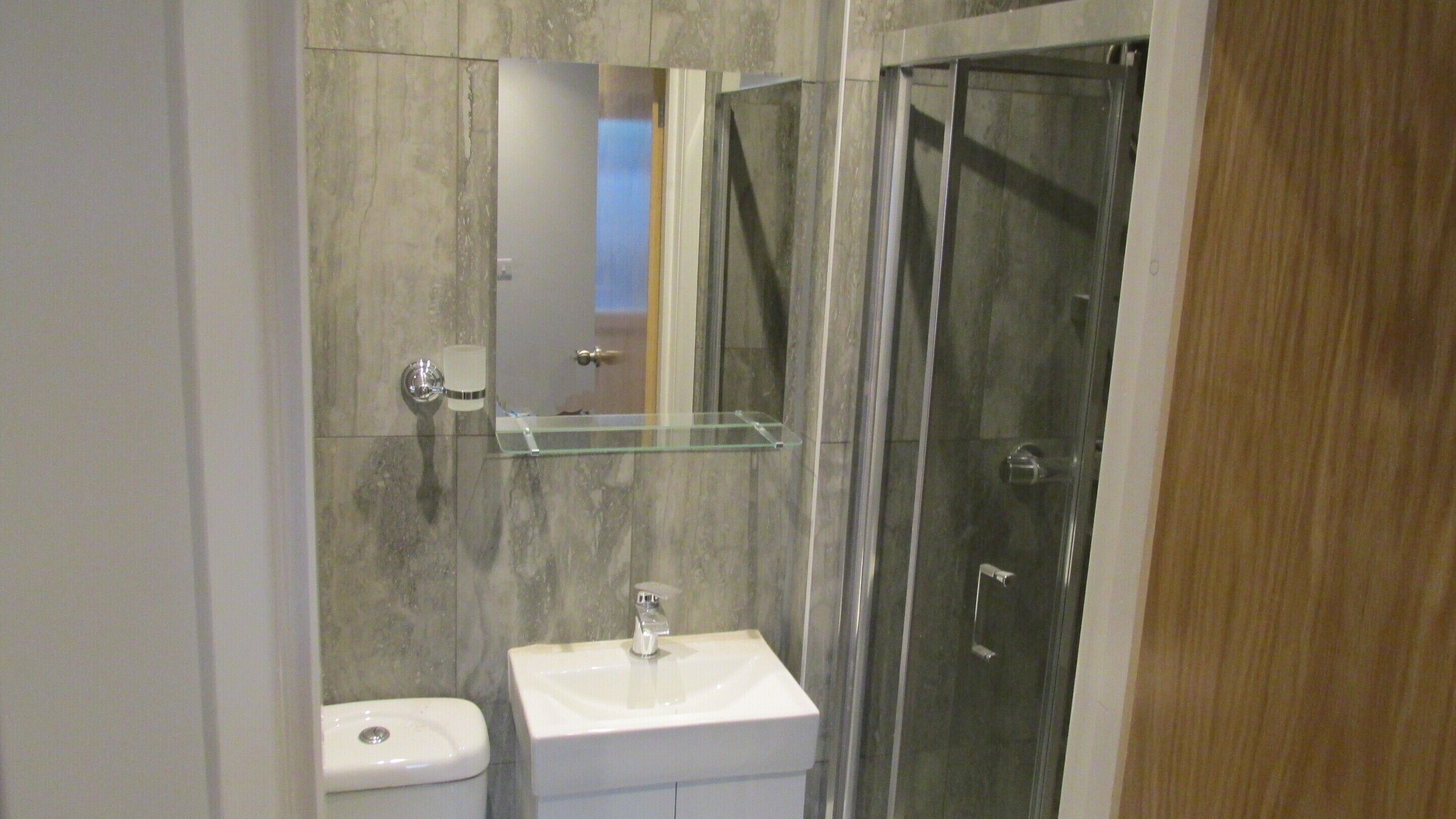 A bathroom with a glass shower enclosure, a white sink, and a toilet.
