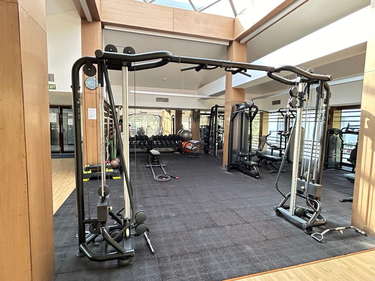 Een fitnessruimte met diverse trainingsapparaten, waaronder krachttoestellen en dumbbells, in een ruime ruimte met hoge plafonds en natuurlijk licht.