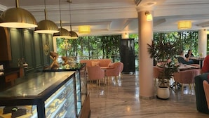 A hotel lobby with a marble floor, a glass display case, pink chairs, and a large potted plant.