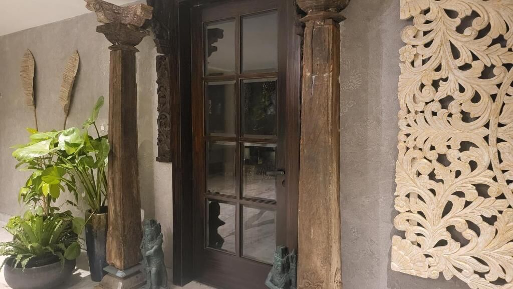 A wooden door with glass panels, flanked by two columns and a decorative panel with intricate carvings.