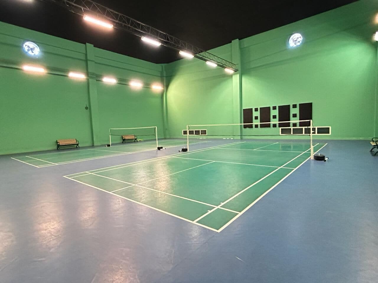 An indoor tennis court with green walls and a blue floor, benches, and a net.