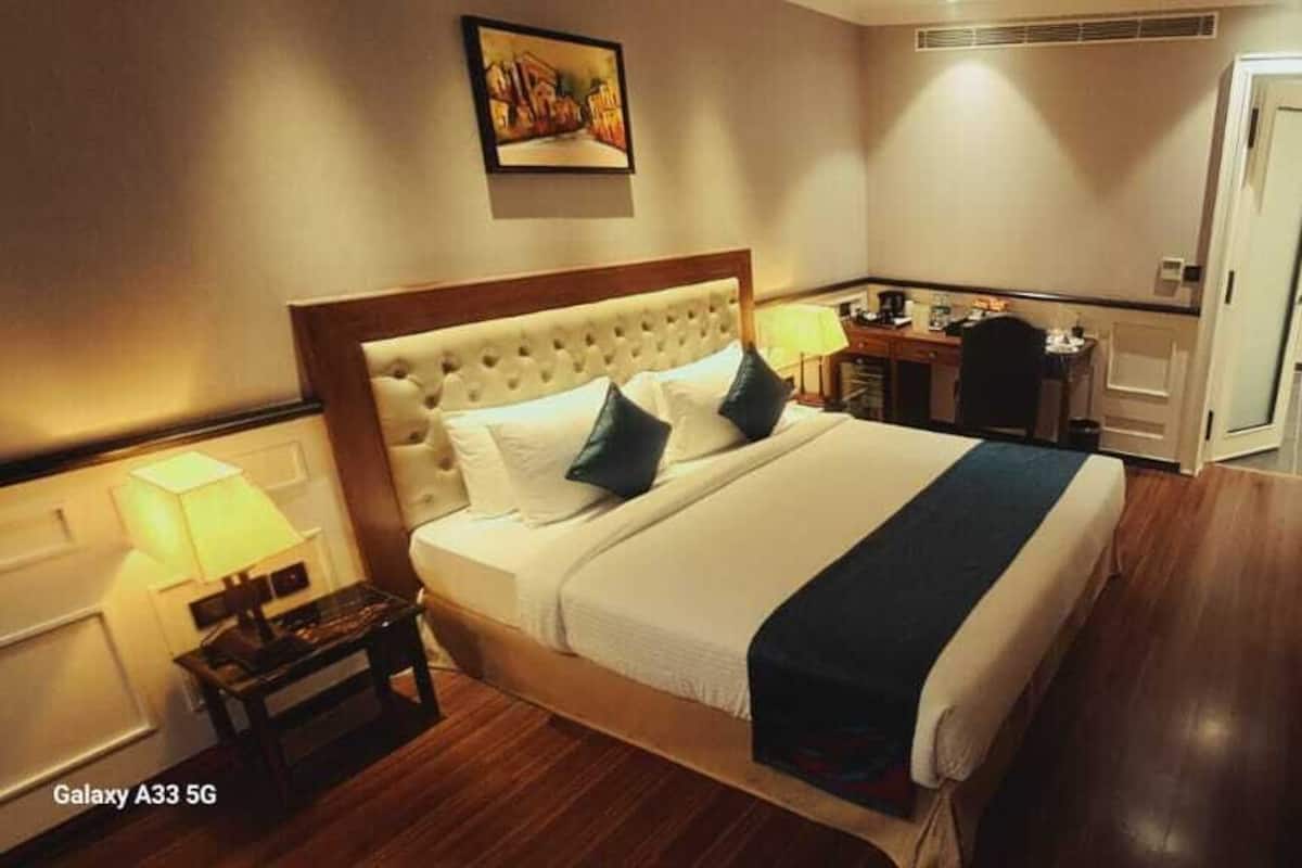 A hotel room with a large bed, a desk, a chair, a lamp, and a picture on the wall.