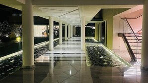 A spacious indoor corridor with marble flooring, white columns, and a central water feature.