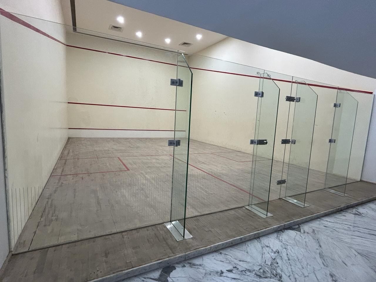 A squash court with glass walls and a wooden floor.