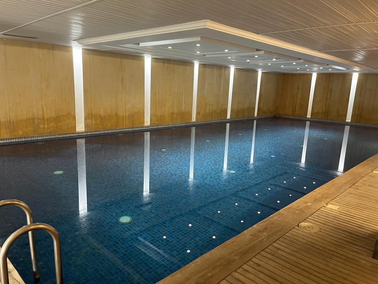 An indoor swimming pool with clear water, wooden walls, and a tiled floor.