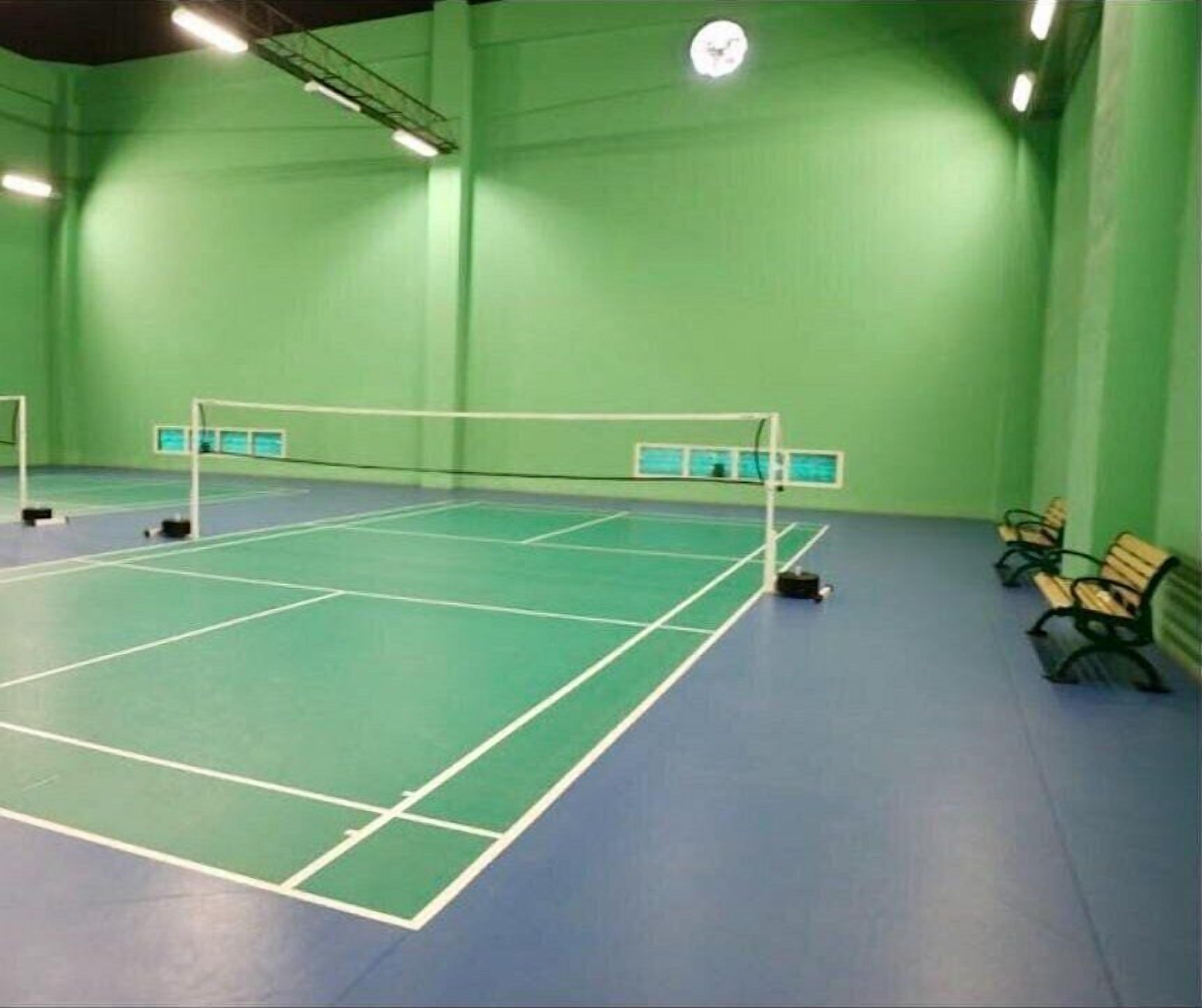 Una cancha de tenis interior con paredes verdes y suelo azul, bancos a lo largo de un lado y una red en el centro.
