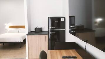 A compact hotel room with a bed, a small kitchenette, a dining area, and a large mirror.