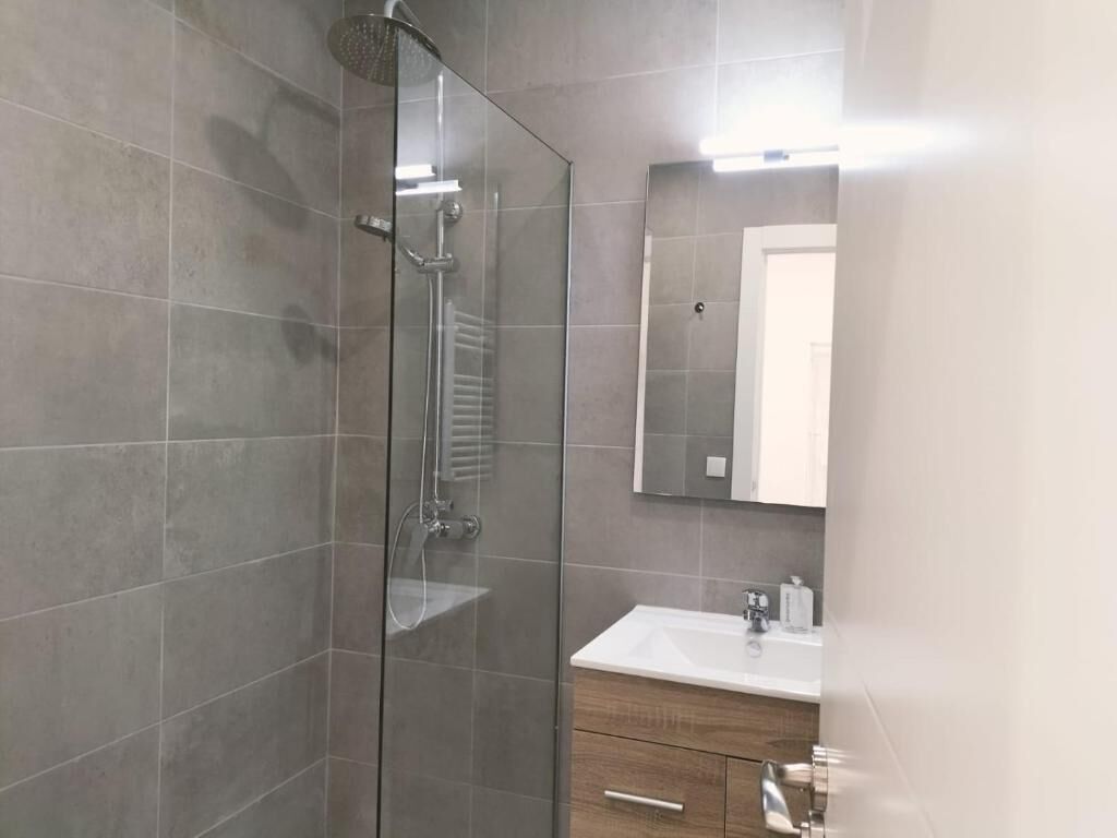 A modern bathroom with a glass shower enclosure, a white sink, and a mirror.