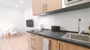 A modern kitchen with wooden cabinets, a black countertop, a stainless steel sink, and a microwave above the counter. - Apartamentos La Brava by gaiarooms  (Salamanca)