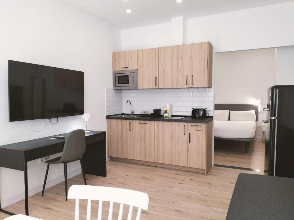 Cocina compacta con microondas, pileta y cocina. Hay un comedor con mesa y sillas, y un televisor colocado en la pared.
