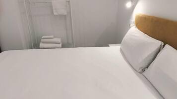 Habitación de hotel con cama, cabecero y zona de ducha con toallas.