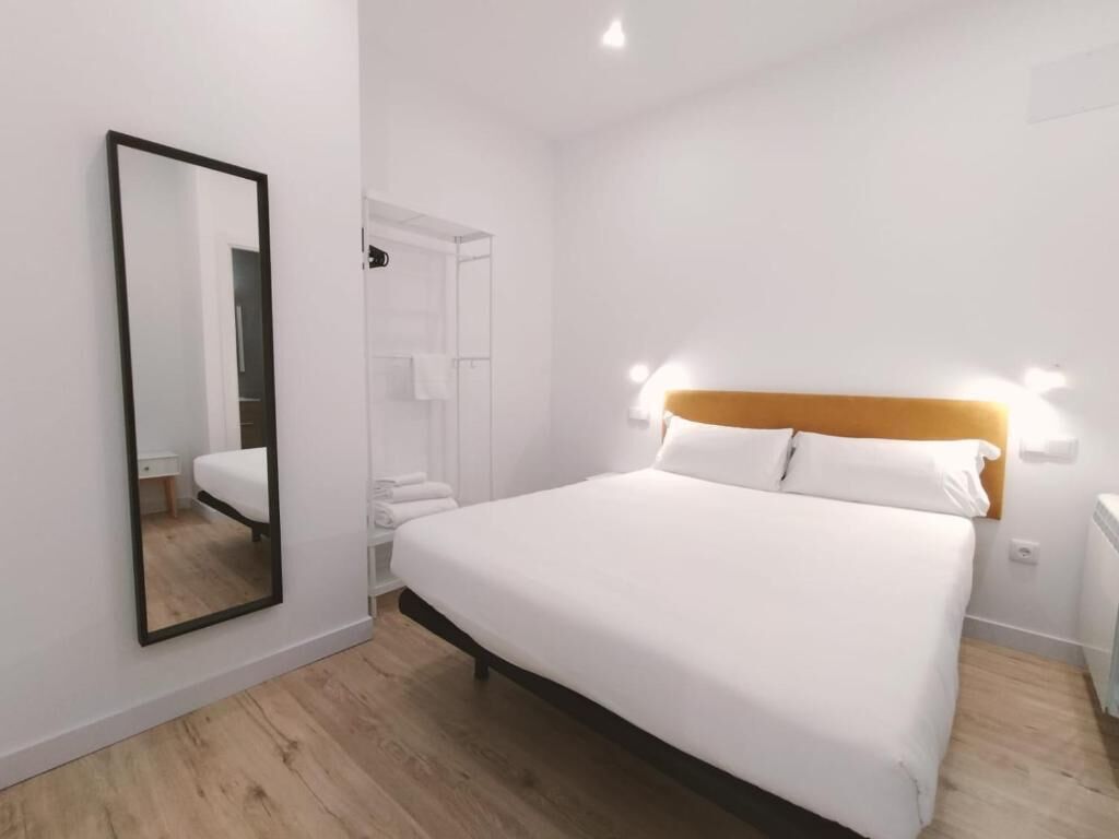 A hotel room with a large bed, a mirror, a wardrobe, and a bedside table.