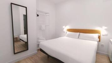A hotel room with a large bed, a mirror, a wardrobe, and a bedside table.