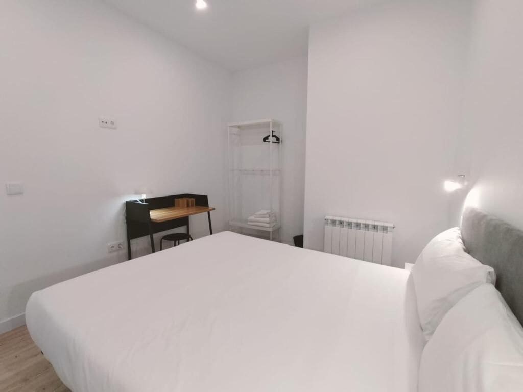A bedroom with a large bed, a desk, a radiator, and a hanging light fixture.