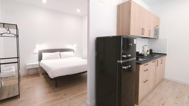 A compact kitchen with a black refrigerator, wooden cabinets, and a microwave. - Apartamentos La Brava by gaiarooms  (Salamanca)