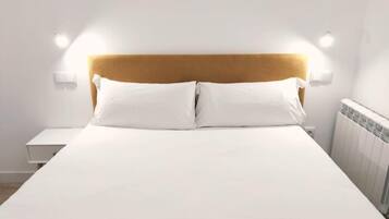Een net opgemaakt bed met een houten hoofdbord, witte beddengoed en twee wandlampen aan weerszijden.