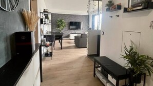 Un salon moderne avec un canapé noir, une table à manger et un coin cuisine équipé d’un téléviseur et d’étagères.
