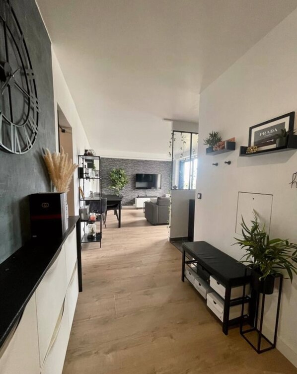 A modern living room with a black sofa, a dining table, and a kitchen area with a TV and shelving.