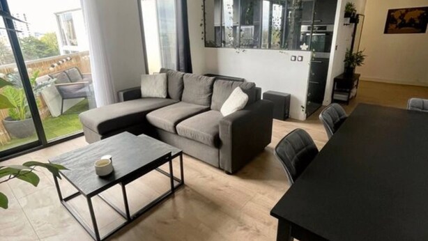 Un salon moderne avec un canapé d’angle, une table à manger et une grande fenêtre donnant sur l’extérieur.