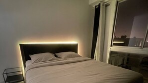 Une chambre moderne avec un grand lit, une table de chevet et une fenêtre donnant sur la ville.