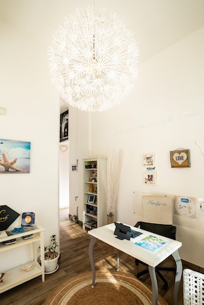 Una habitación con un escritorio blanco, una lámpara colgante y una estantería.