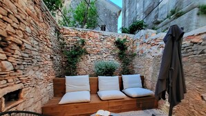 A stone-walled outdoor seating area with a wooden bench and cushions, a round table with a book and snacks, and a chair. - Casa Al Campanile for Your Relaxing Experience in a Rare Cocktail Pool (Vodnjan)