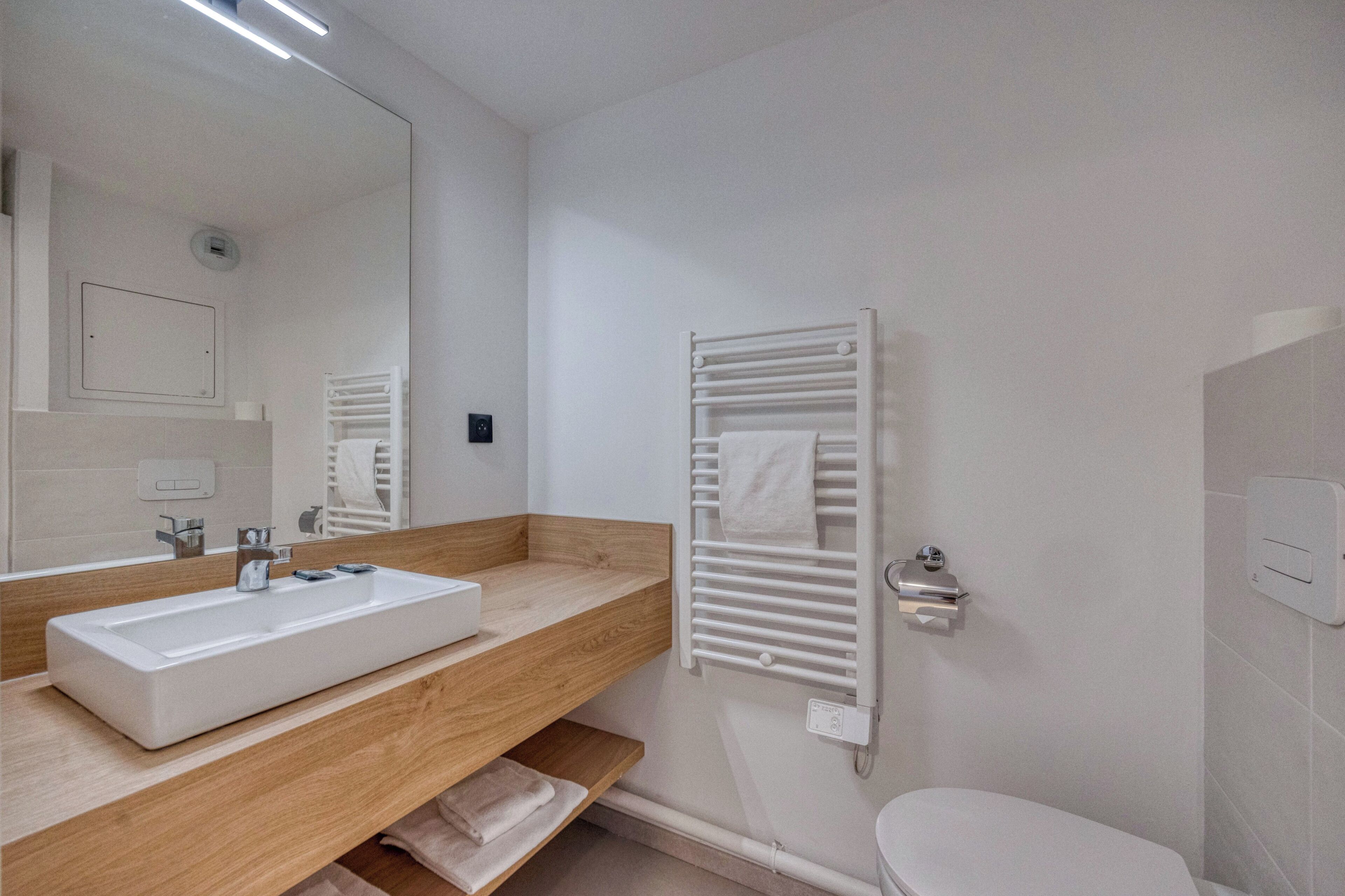Une salle de bain moderne avec un grand miroir, un lavabo rectangulaire, un porte-serviettes et des toilettes.