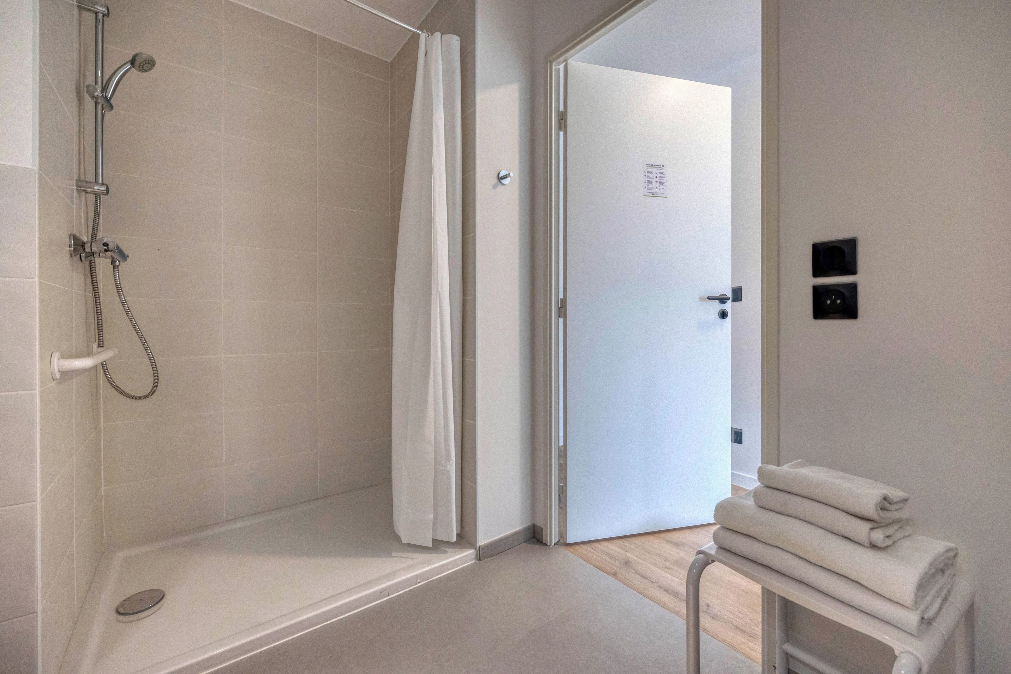 A modern bathroom with a shower, a toilet, and a towel rack with folded towels.
