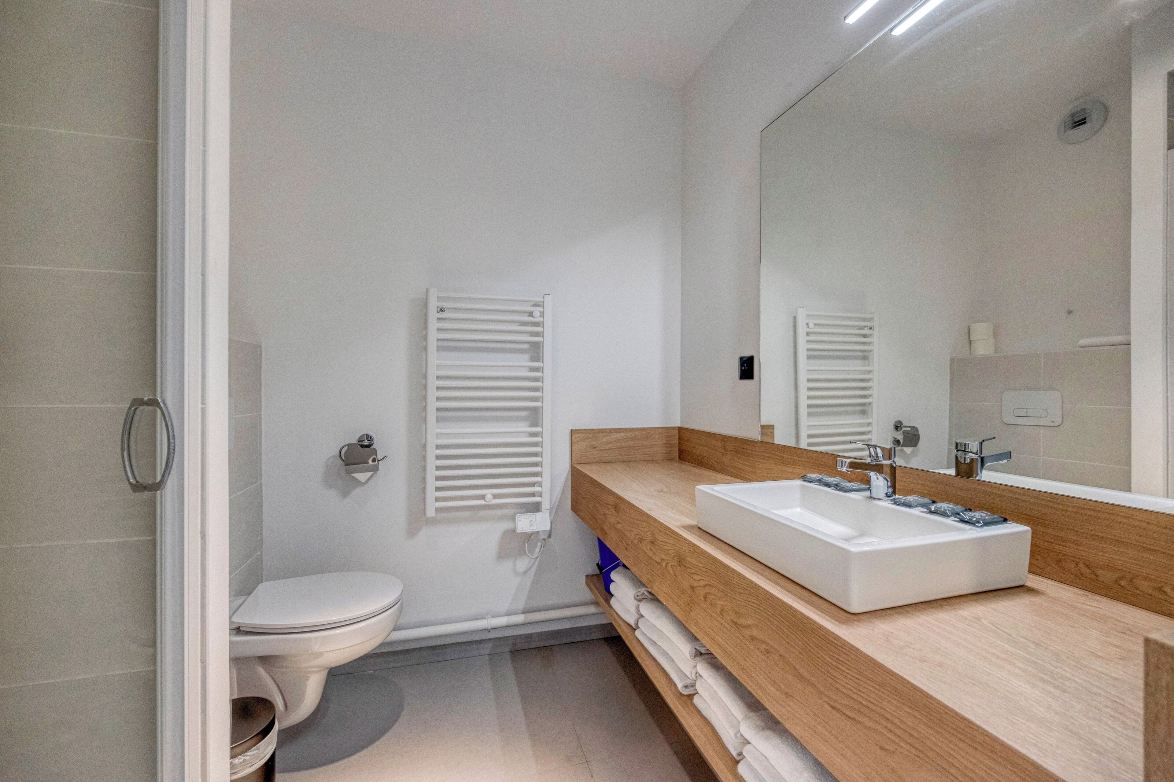 A modern bathroom with a white toilet, a large mirror, and a wooden vanity with a white sink.