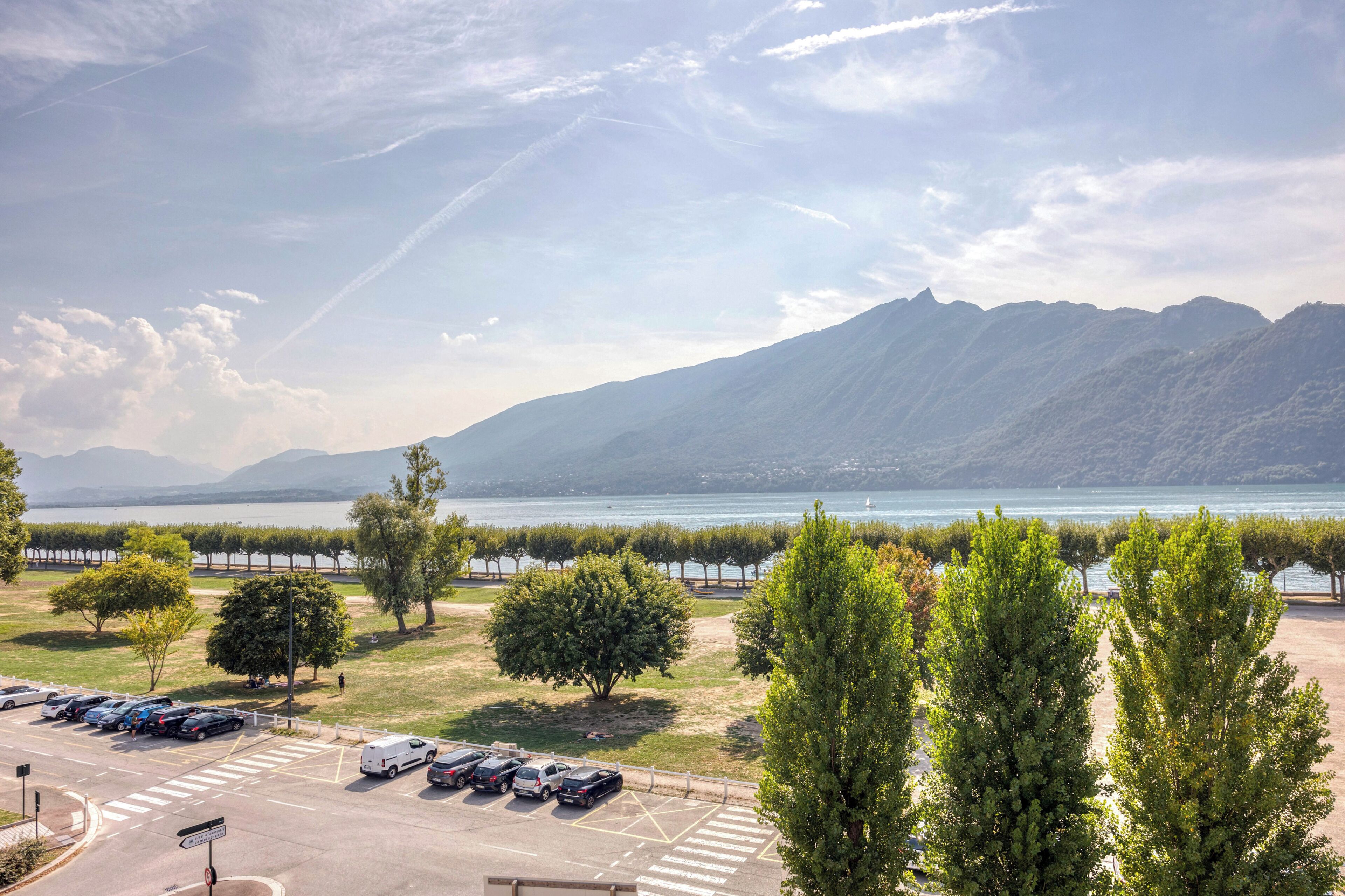 A parking lot with cars, trees, and a view of mountains and a lake.