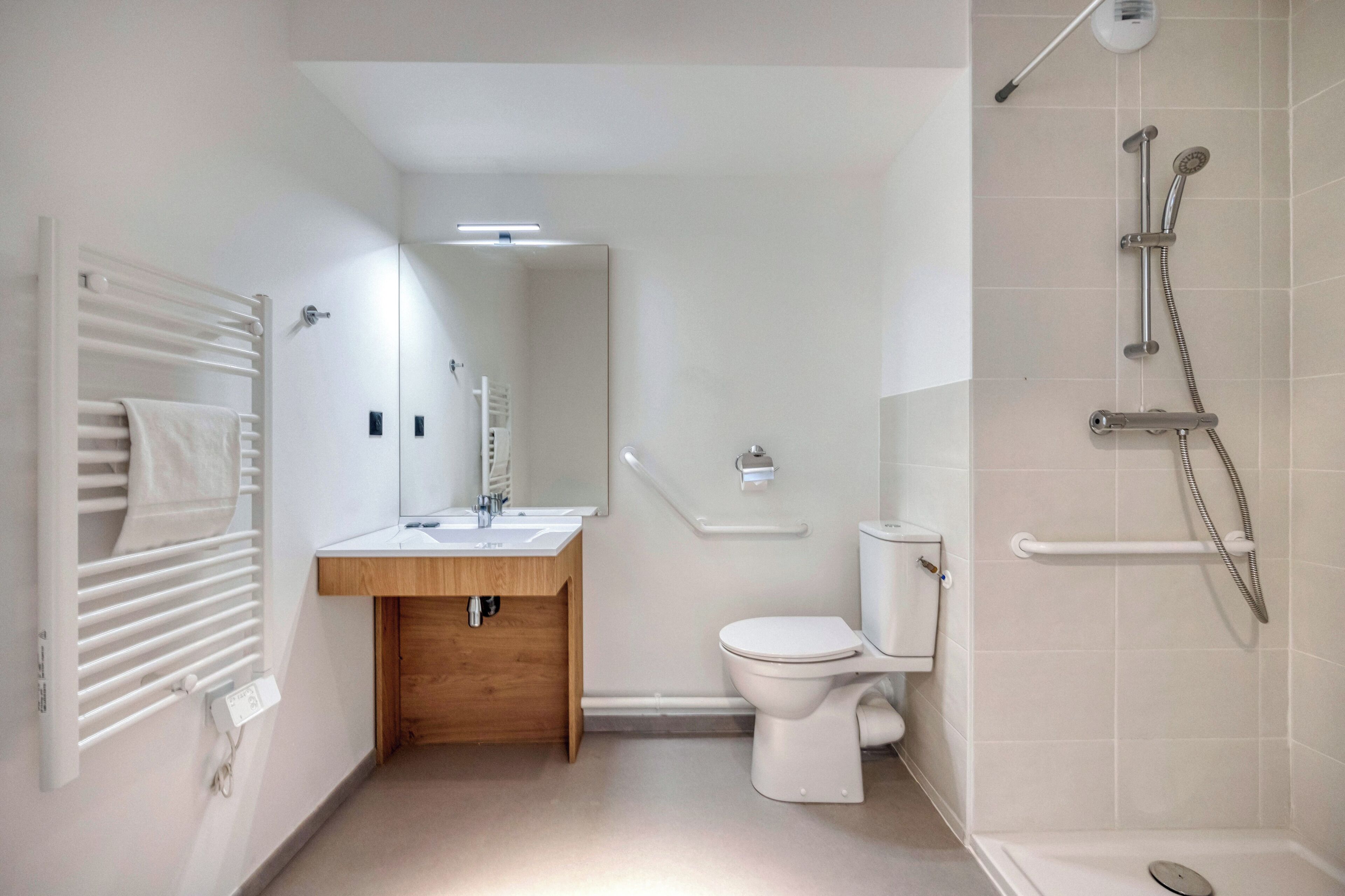 Un bagno moderno con il water bianco, un mobile lavabo in legno, uno specchio e uno spazio doccia con soffione manuale.
