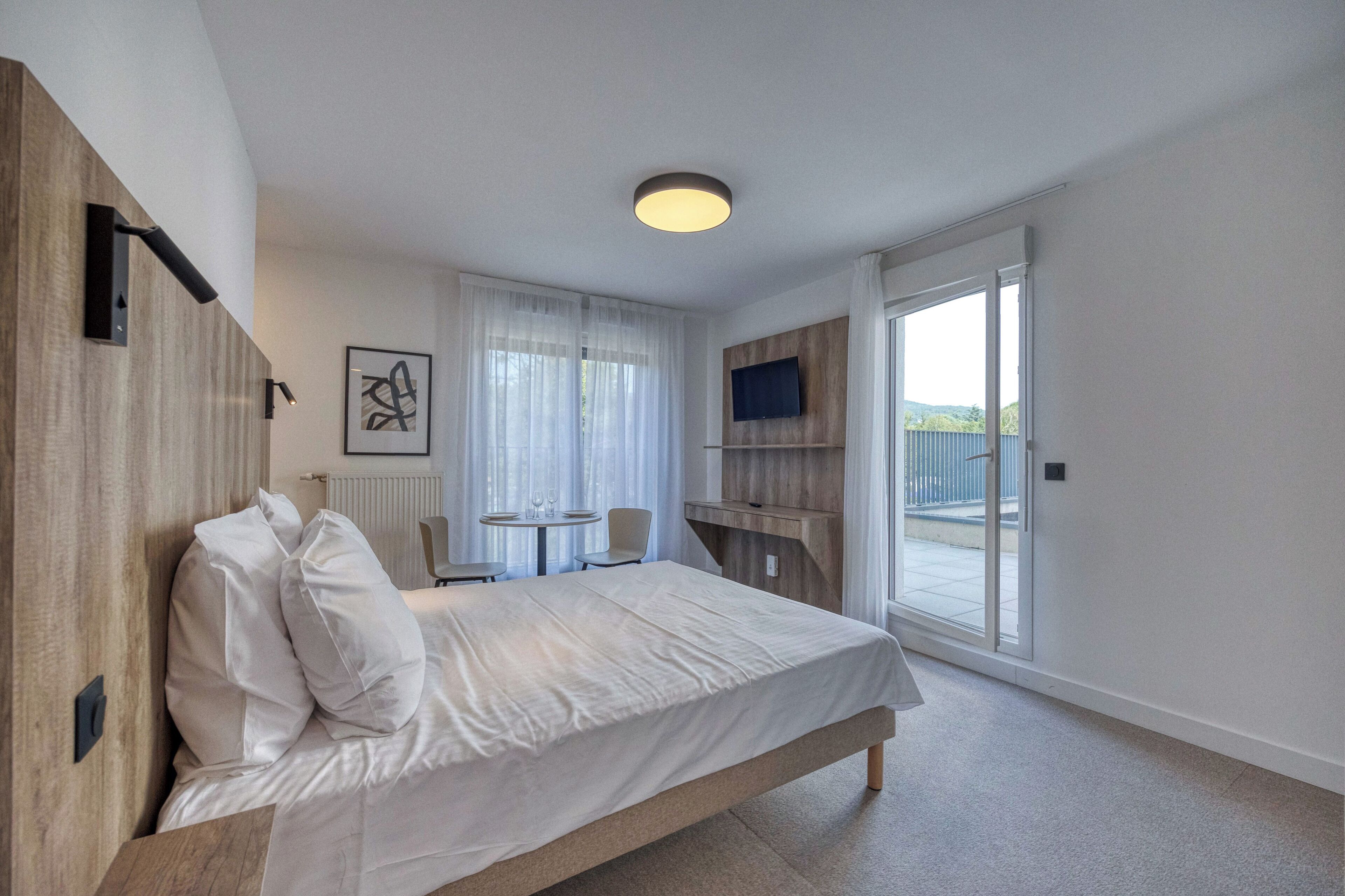 Une chambre à coucher moderne, avec un grand lit, une petite table, une chaise et un téléviseur fixé au mur.