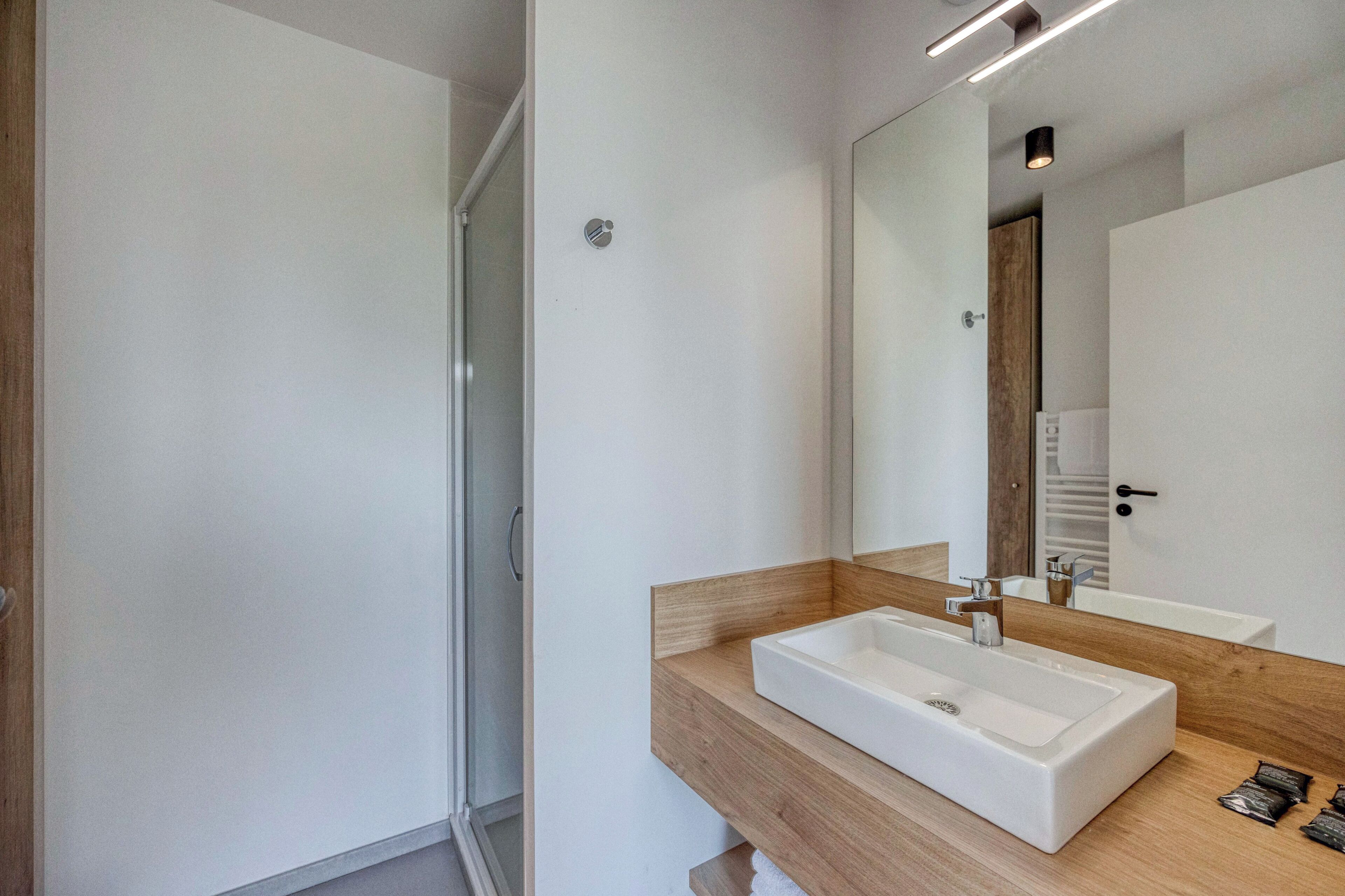 A modern bathroom with a white sink, wooden vanity, and a large mirror.