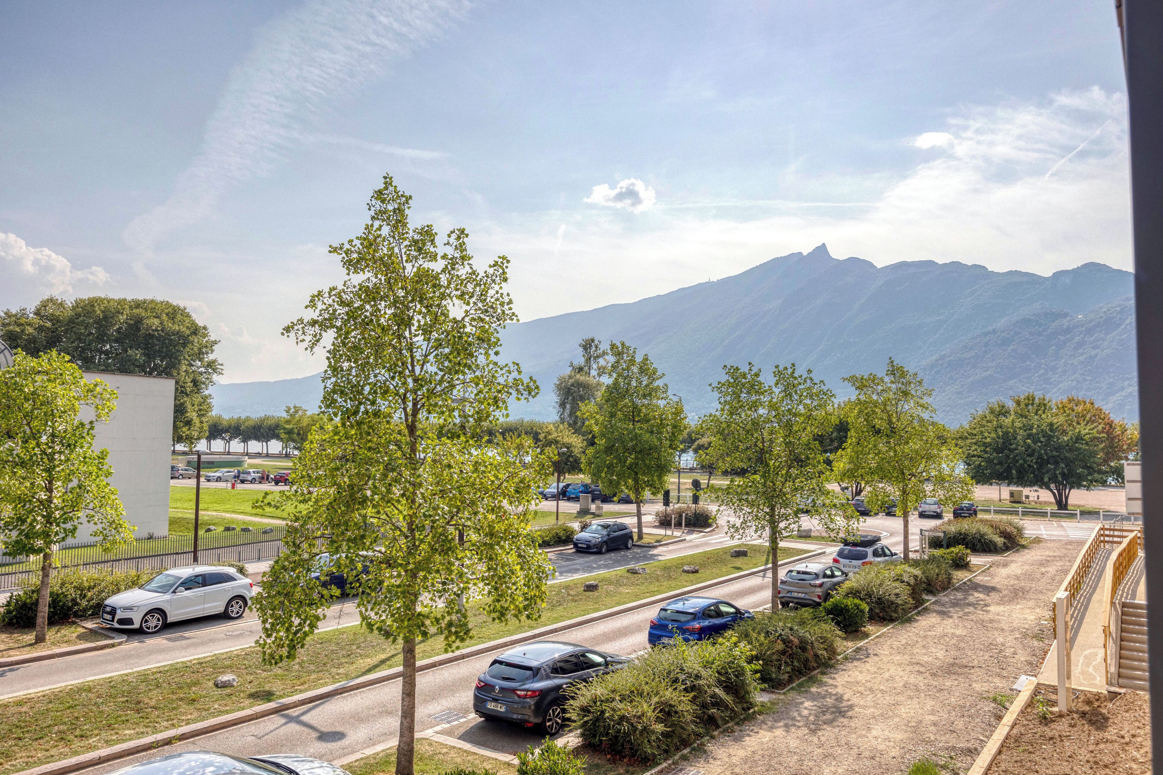 A parking area with multiple cars, trees, and a mountain in the background.