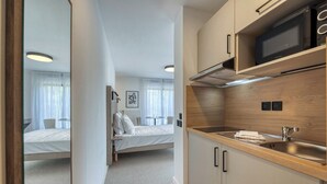 A modern hotel room with a bed, a small kitchenette, and a bathroom.